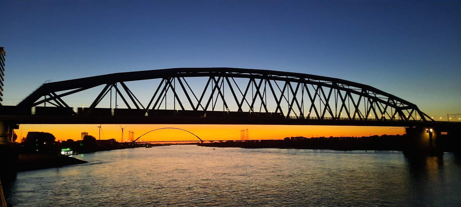 Spoorbrug Nijmegen bij zonsondergang met de Oversteek op de achtergrond