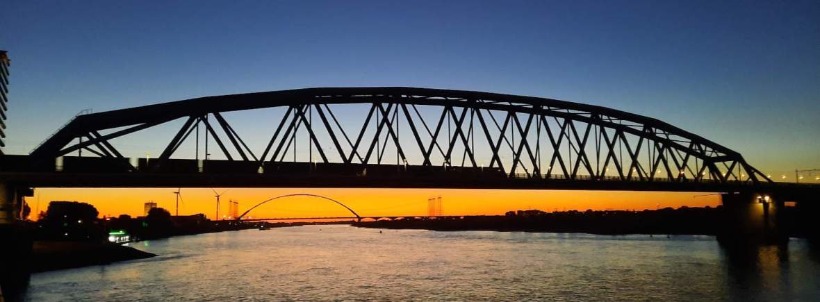 Spoorbrug Nijmegen bij zonsondergang met de Oversteek op de achtergrond