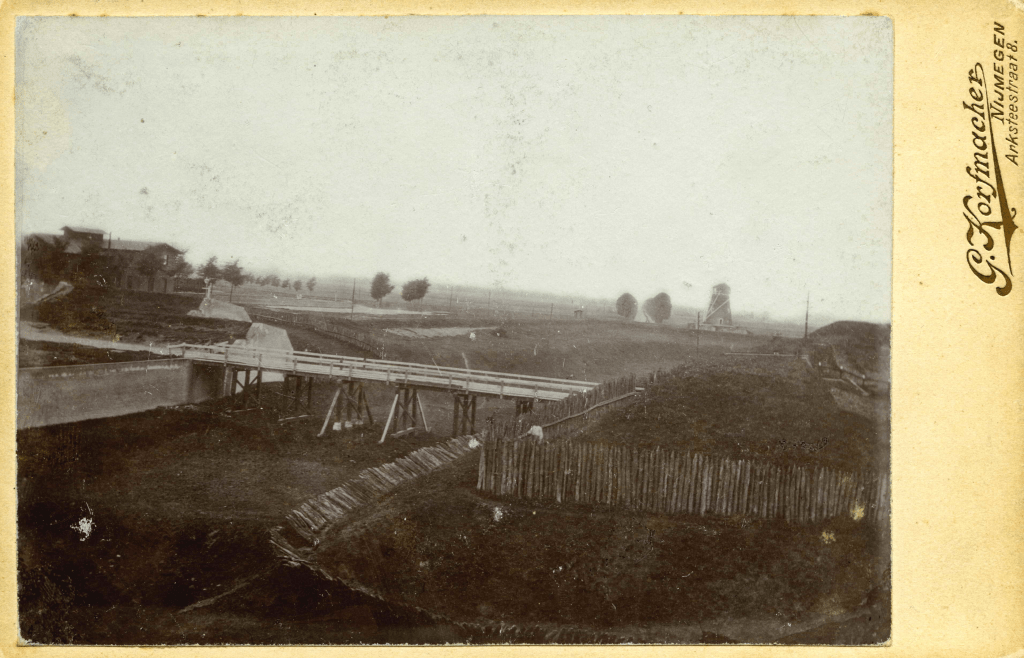 De tweede houten brug buiten de Molenpoort over de droge gracht ter hoogte van het huidige Keizer Karelplein, met links het Station van de spoorlijn Nijmegen-Kleef, de 'Kleefschebaan' (op de plek van het huidige Concertgebouw de Vereeniging), 1875 (Gerard Korfmacher, RAN F23031)