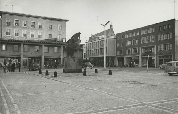 Het pand rechts is juwelier J.H. Courbois. Het 'Oorlogsmonument voor de Nederlandse militairen uit het Rijk van Nijmegen, gevallen in de Tweede Wereldoorlog' , gemaakt door Jac Maris (1951) (op een nieuwe sokkel) ; Op de achtergrond de St. Petrus Canisiuskerk in de Molenstraat. Links de zaak van Holla's kledingsmagazijn. Rechts naast de winkel van Theo Seegers de juwelier J.H. Courbois en links van Theo Seegers de slagerij van P.W. Boukes ; Op de hoek met de Molenstraat de zelfbedieningswinkel van Jansen-Hendriks, 1954-1955 (F42032 RAN collectie KNBLO, auteursrecht J.F.M Trum CC-BY-SA)