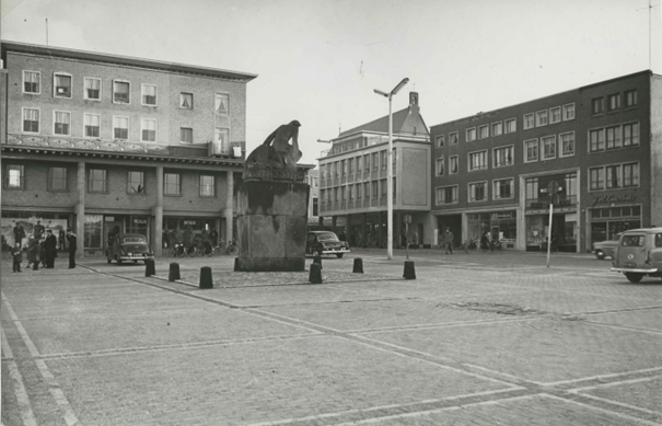 Het pand rechts is juwelier J.H. Courbois. Het 'Oorlogsmonument voor de Nederlandse militairen uit het Rijk van Nijmegen, gevallen in de Tweede Wereldoorlog' , gemaakt door Jac Maris (1951) (op een nieuwe sokkel) ; Op de achtergrond de St. Petrus Canisiuskerk in de Molenstraat. Links de zaak van Holla's kledingsmagazijn. Rechts naast de winkel van Theo Seegers de juwelier J.H. Courbois en links van Theo Seegers de slagerij van P.W. Boukes ; Op de hoek met de Molenstraat de zelfbedieningswinkel van Jansen-Hendriks, 1954-1955 (F42032 RAN collectie KNBLO, auteursrecht J.F.M Trum CC-BY-SA)