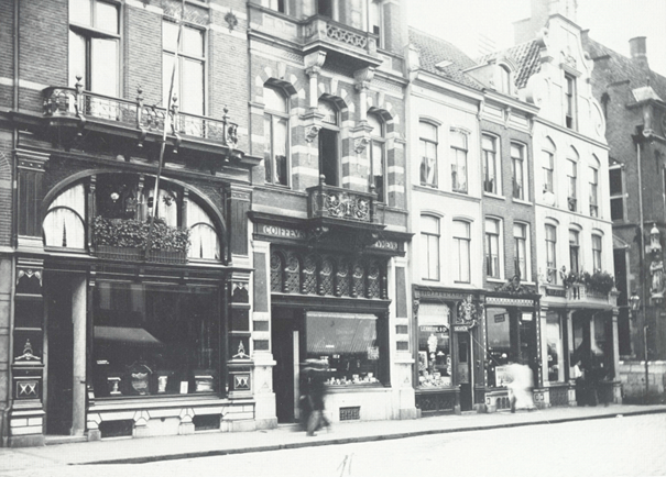 Winkelpanden aan de zuidzijde van de Burchtstraat: v.l.n.r. C.J. Kleber (marchand-tailleur) (Lange Burchtstraat 10) , Firma J.A.G. Scheerder en Co. Coiffeur architect Weve (Lange Burchtstraat 8), Sigarenmagazijn Lehmkuhl en Co. (Lange Burchtstraat 6), Wijnhandel Brendel en Zoon (Lange Burchtstraat 4) en Patisserie Confiseur en Cuisinier Rups (Lange Burchtstraat 2), 1910 -> nog een verbouwing geweest?