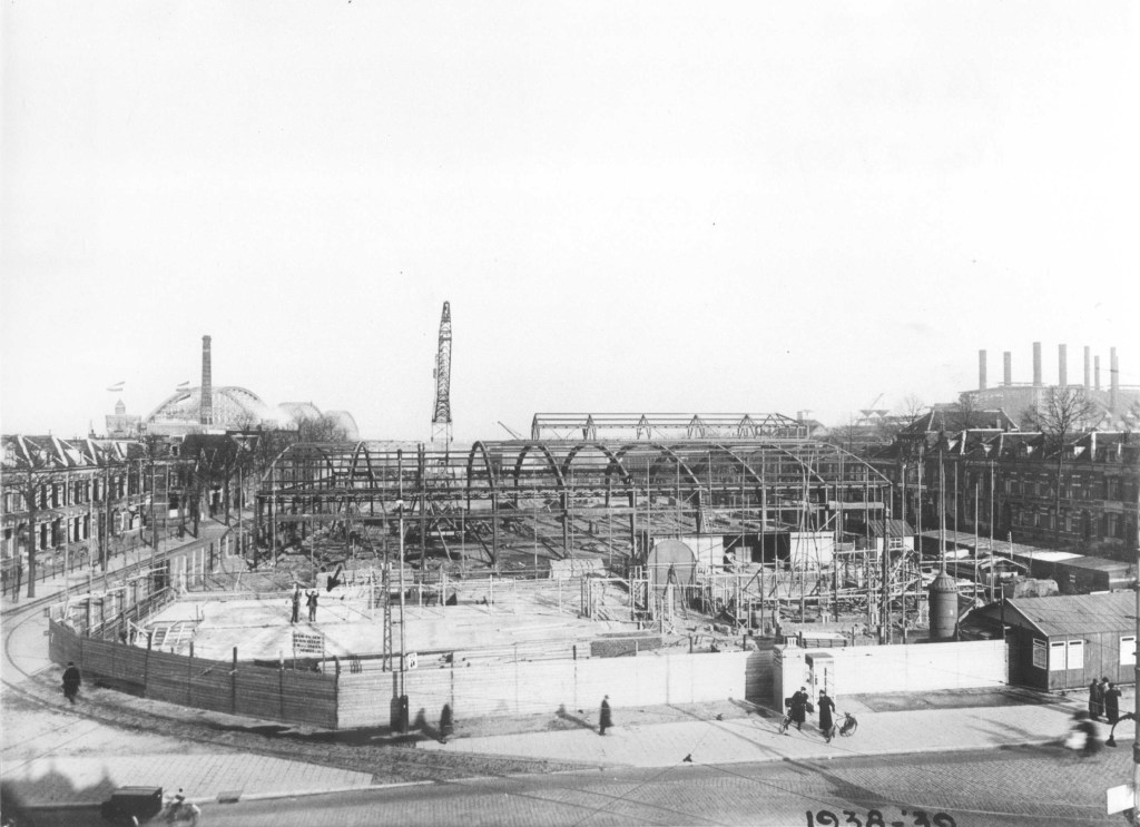Het in aanbouw zijnde pand van Terminus en de veehallen, links en rechts de huizen aan de Nieuwe Markt, op de achtergrond links de Spoorbrug en rechts de oude elektriciteitscentrale aan de Waal, 1938-1939 (F29359 RAN)