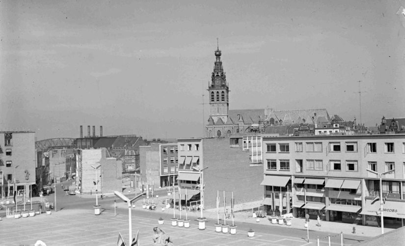 Gezicht op de noordzijde met v.l.n.r. Café Restaurant Royal (van A.A. Raafs, Plein 1944 nr. 128), Lunchroom annex Banketbakkerij Pleinzicht (van W.P.H.A. Cornelissen, nr. 135), Sigarenmagazijn H.W.R. Brans (nr. 136), Juwelier en Horloger A.J. Janssen (nr. 137) en P. Jacobs Textiel en Tricotage (nr. 140); in het midden de St. Stevenstoren, 1954 (GN8809 RAN)
