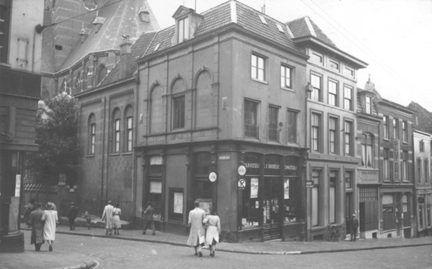 Het derde pand, met openstaande deur, is dat van Geertsen: Links de Augustijnenstraat en rechts de Stikke Hezelstraat , met op de hoek de Drukkerij en Boekbinderij Richelle en rechts daarvan o.a. de panden van Herman Geertsen en de Slijterij Oporto ; geheel links de Augustinuskerk, 1/9/1941 (F34009 RAN)