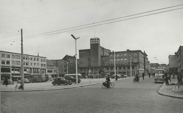 Zicht op de wederopbouw van het plein. Vrnl: Holla's kledingmagazijn, Van der Werff Woninginrichting, parfumerie Albers, foto Verwey, schoenenmagazijn A. Holland, Cafetaria Centrum Expresse, P. Jacobs Textiel, Juwelier A.J. Janssen, Sigarenmagazijn H. Brans en uiterst links Lunchroom Pleinzicht, 1953-1955 (Fotopersbureau Gelderlander,Auteursrechthouder J.F.M. Trum via F42035 RAN CCBYSA)