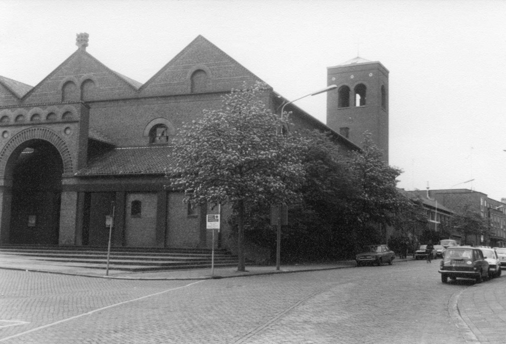 De R.K. O.L. Vrouw van de Berg Carmelkerk aan de Doddendaal, de voorgevel met hoofdingang aan de westzijde en de zuidzijde met de klokkentoren. Kerk en klooster zijn ontworpen in 1951 door Cees Pouderoyen, de klokkentoren dateert uit 1955. Links de afslag naar de Kroonstraat, 5/1980 (Frans Hermans via F24935 RAN CC0)