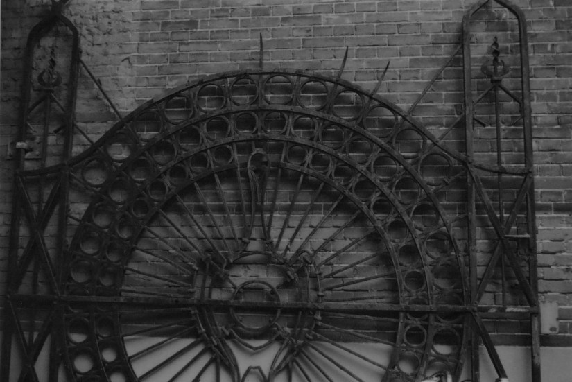 Smeedijzeren hekwerk in de vorm van een pauw ter afsluiting van de doorgang (nu aan de achterzijde) tussen de woningen van Graafseweg 57 en 59. Het gehele blok, van huisnummer 55 tot 61, werd oorspronkelijk gebouwd in 1902 in opdracht van H.H. de Haan als kantoorpand met woningen + magazijn naar ontwerp van de architecten van de(r) Pluijm en Gielen. Het hek werd in 1923 gestolen en is niet meer teruggevonden, (Tineke de Jonge via F88665 RAN CCBYSA)