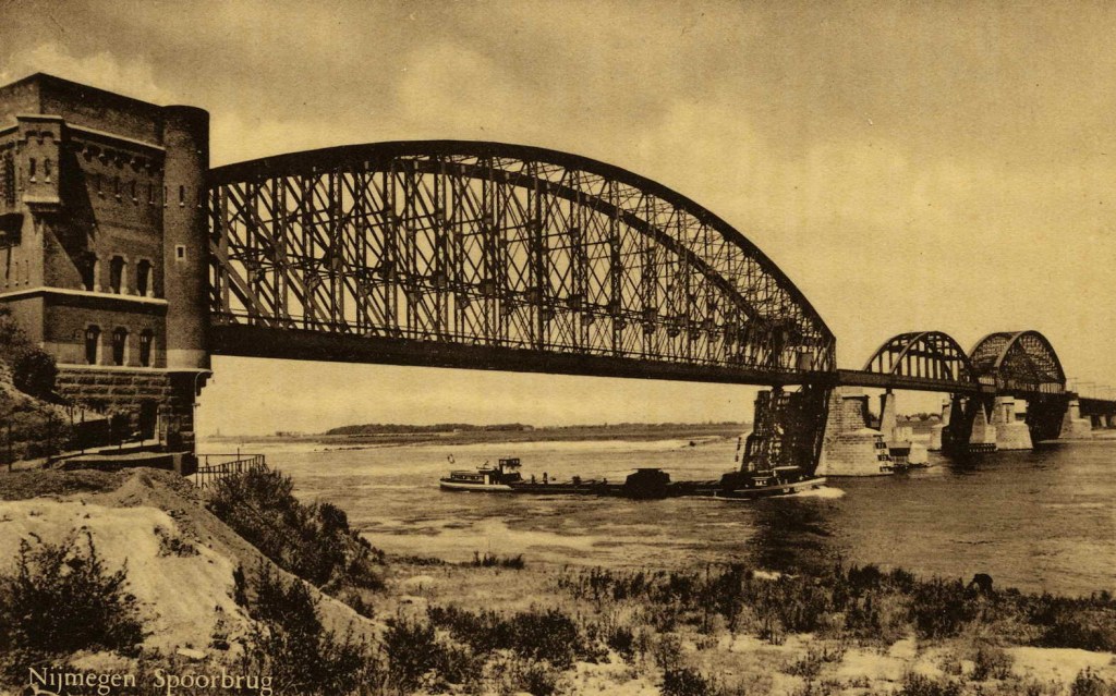 De oude (vakwerk)spoorbrug over de Waal uit 1879 met de twee oorspronkelijke boogoverspanningen en het herstelde tijdelijke brugdeel in het midden. Links, het zuidelijk landhoofd van architect P.J.H. (Pierre) Cuypers (16/05/1827 - 03/03/1921) , 1947-1948 (Maatschappij Rembrandt via F91350 RAN)