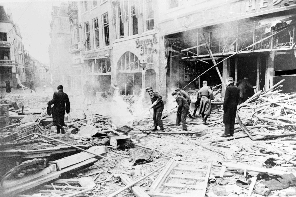 De verwoeste Albert Heijn; Opruimingswerkzaamheden na de verwoestingen van het bombardement 22 februari 1944. Rechts Albert Heijn met links daarvan de Urquelle Stube, na de oorlog Old Dutch geheten, met links daarvan Ockhuizen Lunchroom. Op de achtergrond zichtbaar de splitsing van de Platenmakersstraat (rechts) en de Korte Burchtstraat (links), 22-2-1944 (Gn114 RAN)