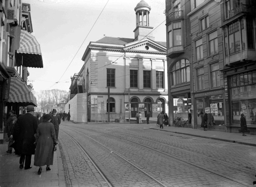 De Schouwburg aan de Oude Stadsgracht 1, kort voor de afbraak; gezien vanuit de Lange Burchtstraat in de richting van het Kelfkensbos. Rechts, op de hoek, uitverkoop van de Damesmodewinkel van Banens en Beermann (waar in 1935 de Manufacturenzaak van J.H. Duives zou worden gevestigd), 1935 (GN8078 RAN)