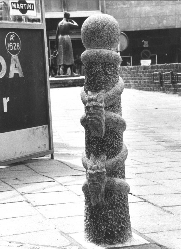 Grote Markt / Vijfringengas : Afsluitpaal voorstellende Moenen en vijf ringen, in 1974 vervaardigd door Giuseppe Roverso. De hardstenen paal is versierd met 5 ringen, die aan elkaar worden geschakeld door duivelskoppen. De ringen verwijzen naar de naam van het gasje, terwijl de duivelskoppen een verwijzing zijn naar het beroemde verhaal van Mariken van Nimwegen. Roverso was van oorsprong een Italiaanse beeldhouwer, geboren in 1900 in Chiampo en overleden in 1977 te Nijmegen, 1976 (Jan Cloosterman via F1481RAN CCBYSA)