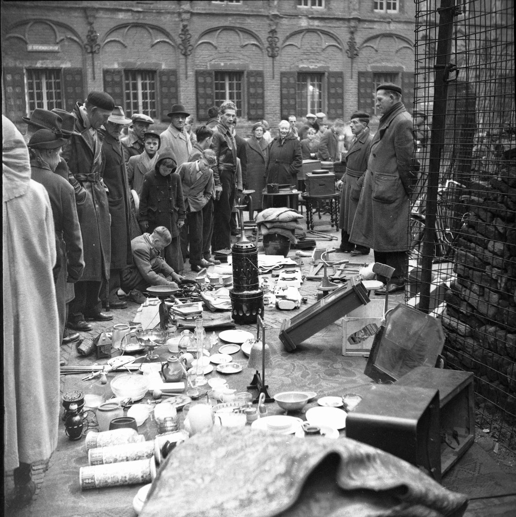 In ieder geval sinds 1913 vond de uitdragersmarkt, in Nijmegen algemeen bekend als de luizenmarkt, of op zijn Nimweegs luusemert, met korte onderbrekingen tot op heden plaats aan de voet van de Sint Stevenstoren. Op de achtergrond de Latijnse School, 1945-1955 (1945-1955 Auteursrecht: J.F.M. Trum via VN17136 RAN CCBYSA)