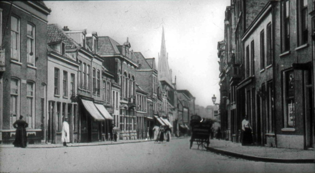 Links een stukje hoekgebouw van de eerste Walstraat : het latere Hotel, Café-Restaurant 't Rondeel van Van Kempen. Bloemerstraat gezien in de richting van de Augustijnenstraat. Met op de achtergrond de toren van de St. Augustinuskerk, 1890-1895 (Dr. Jan Brinkhoff via D42 RAN CC0)