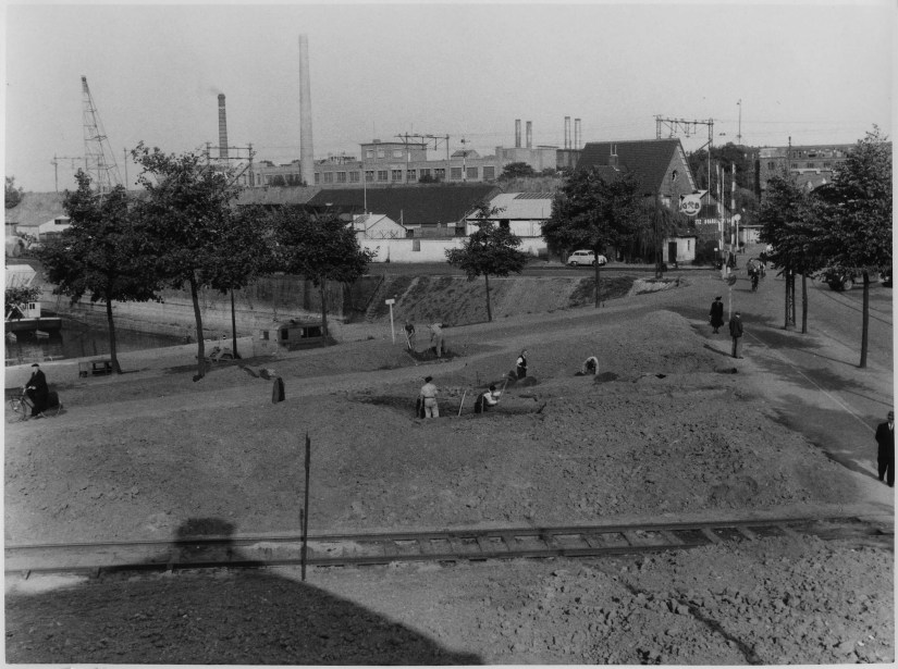 Het havenplantsoen in aanleg, gezien vanaf de Weurtseweg. Op de voorgrond de goederenspoorlijn naar het havengebied, rechts, de Voorstadslaan met de spoorwegovergang en het pand van steenkolen- en brandstoffenhandel J.J. Giesbertz NV. Op de achtergrond, achter de spoordijk in het midden, papierfabriek Schuller aan de Nieuwe Markt, links boven de oude havenkraan op de loswal van de Nieuwe Haven (Waalhaven), 1953 (Foto Grijpink via F88668 RAN CCBYSA)