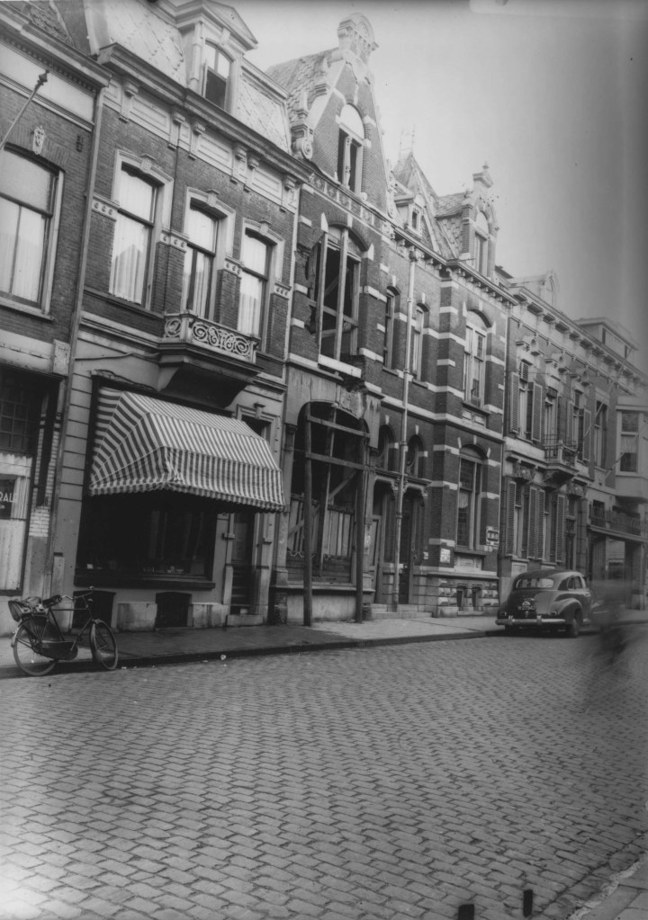 Een aantal winkels met bovenwoningen. Op de ruit bij nummer 38 (geheel links) zijn de laatste letters van "DE SPORTCENTRALE" zichtbaar, het ge(her)opende café van August Lodenstein. Vervolgens nummer 36 met zonnerscherm en het beschadigde pand nummer 34. Daannaast nummer 32 1946-1950 (F28566 RAN)