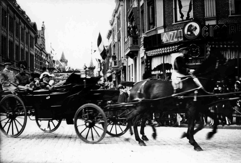 Koningin Wilhelmina en prins Hendrik in Nijmegen (hoek In de Betouwstraat / Molenstraat) bij de opening van het Maas-Waalkanaal; links achter de koets is de hoek Bisschop Hamerstraat/In de Betouwstraat te zien, 27/10/1927 (F66873 RAN)
