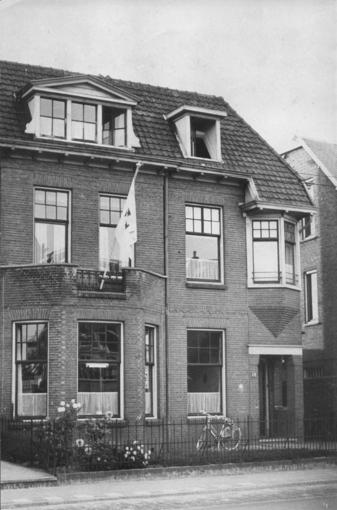 Twee onder één kap in 1916 gebouwde herenhuizen door aannemer/architect gebroeders Haspels. Er woonde onder andere een dominee; het pand biedt al geruime tijd onderdak aan de Internationale Bouworde, een katholieke stichting die jonge vrijwilligers inzet bij sociale bouwprojecten wereldwijd. De vlag die uithangt is waarschijnlijk de vlag van de stichting, foto 1-10-1959 (Fotopersbureau Gelderland via F11370 RAN CCBYSA Auteursrechthouder J.F.M. Trum) 1916 oa St. Annastraat 172 Galgenveld