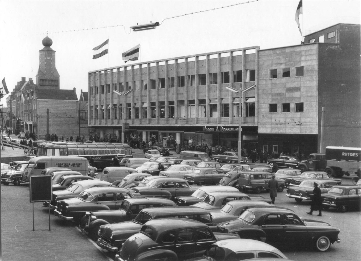 Vanuit onder de Kerkboog in de richting van het pand van Vroom & Dreesmann. Dit pand ligt aan de Grote Markt. Vroom en Dreesmann is er al een tijd niet meer. Op 31 december 2015 werd het bedrijf failliet verklaard, 1954-1955 (Foto Grijpink via F14236 RAN CCBYSA)