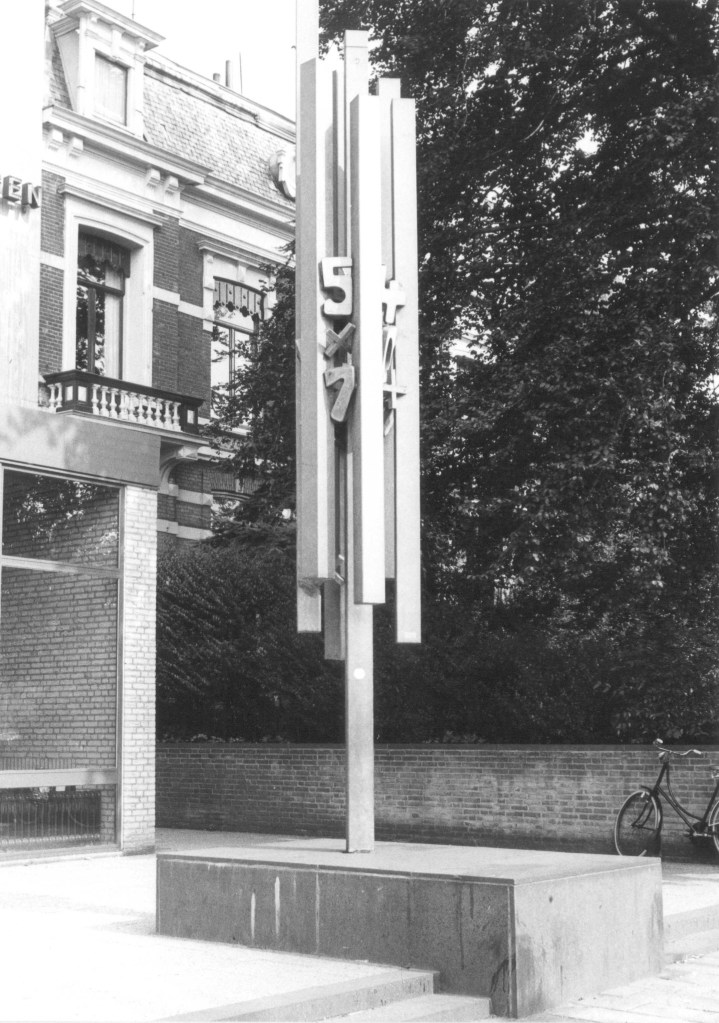 Zuil met cijfers (uit 1974) : een metaalreliëf met symbolen die in het geldverkeer gebruikt worden, vervaardigd door Jac Maris ; het reliëf is geplaatst voor de Rabobank. Achter het kunstwerk nog te zien de villa van Tandarts Roosen, in 1977 afgebroken voor de bouw van het Verzekeringskantoor Bovemij ; Oorspronkelijk Keizer Karelplein; het kunstwerk is spoorloos verdwenen, 1975 (Frans Kup via F14638 RAN CCBYSA)