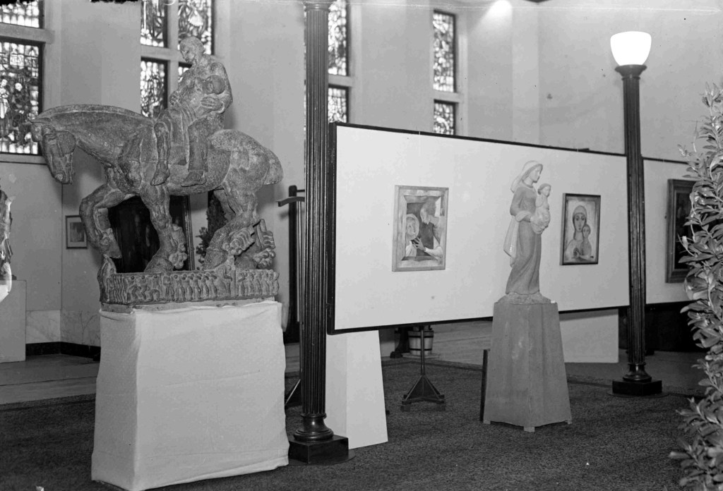 Links het beeld De Barmhartige Samaritaan, gemaakt door Jac Maris op een tentoonstelling van religieuze kunst in de raadszaal in het Stadhuis Nijmegen. Tegenwoordig te vinden op het Vrijheidsplein / Niersweg te Gennep, 1950 (GN4190 RAN)