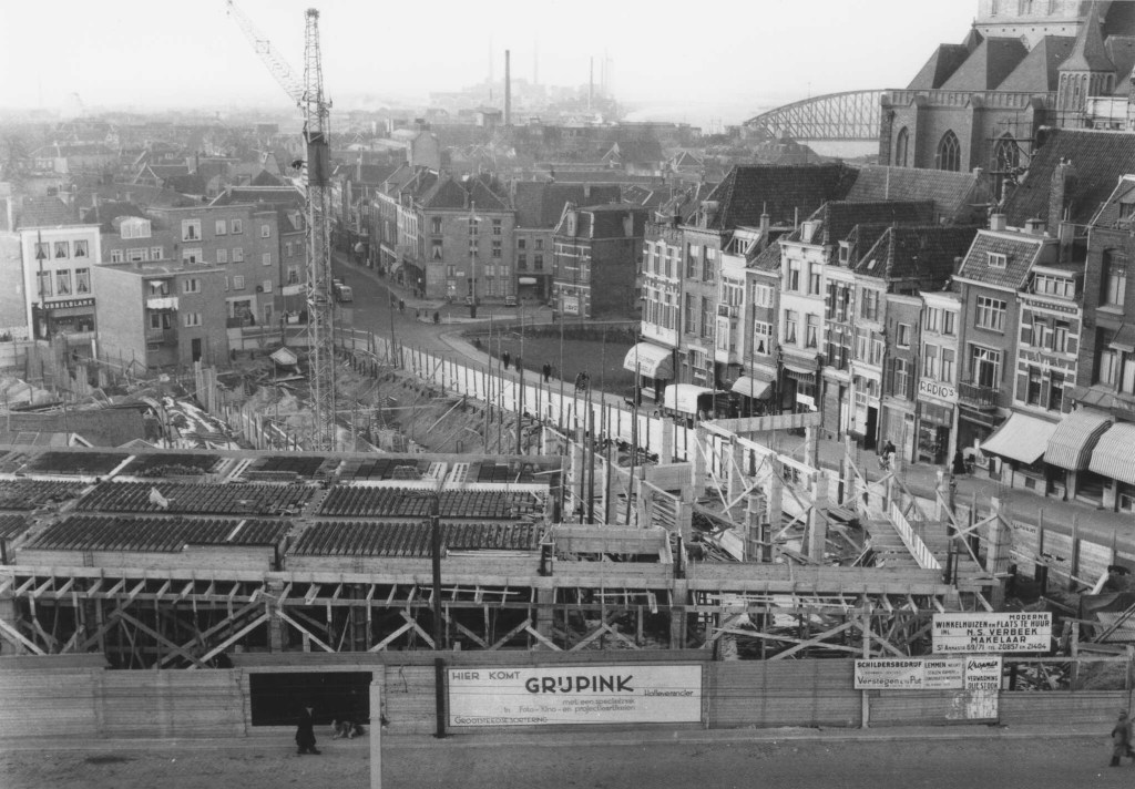 Het complex in aanbouw: de herbouw van een aantal winkelpanden aan de Stikke Hezelstraat - Augustijnenstraat. Op de achtergrond links panden aan de Houtstraat en in het midden aan de Ganzenheuvel, 1955 (Foto Roozenboom via F58609 RAN CCBYSA)