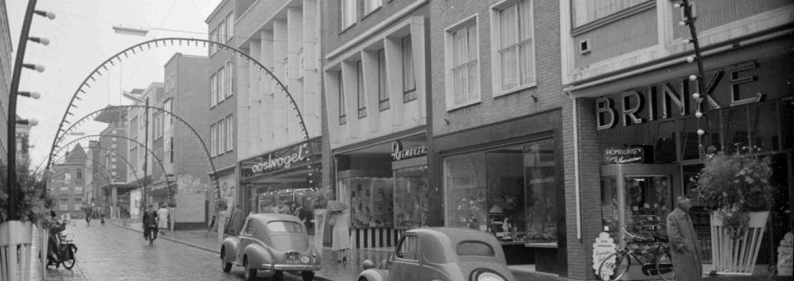 Gezicht op de oostzijde van de Broerstraat met de winkelpanden van o.a. (v.r.n.l.) Slagerij Brinke (op de hoek met het Kerkegasje), Parfumerie Au Printemps, Schoenenzaak Gebrs. Raemakers, Herenmodezaak Oostvogel en de bouw van de panden van Jamin en Schoenenzaak BATA ; bovenaan het nieuwbouwpand van de Herenmodezaak Van Dijk & Witte (Burchtstraat 2, geopend op 21 september 1955), 1955 (GN3877 RAN)