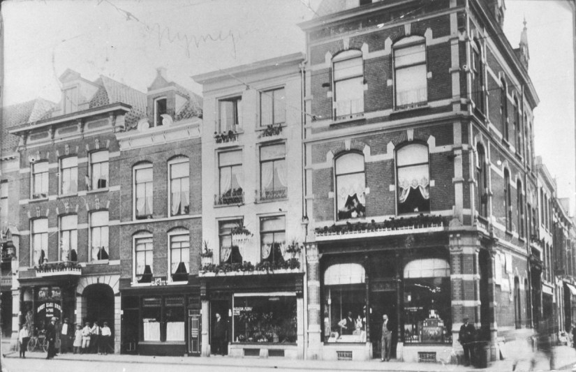 Gezien vanaf het Valkhofplein, rechts de Hertogstraat. In het midden Bloemen-Magazijn "Flora" van bloemist T. van den Brink. Links achter het groepje kinderen zichtbaar de Hel of Pastoorsgasje, een doodlopend steegje verdwenen in 1944, 1910-1914 (F17701 RAN)