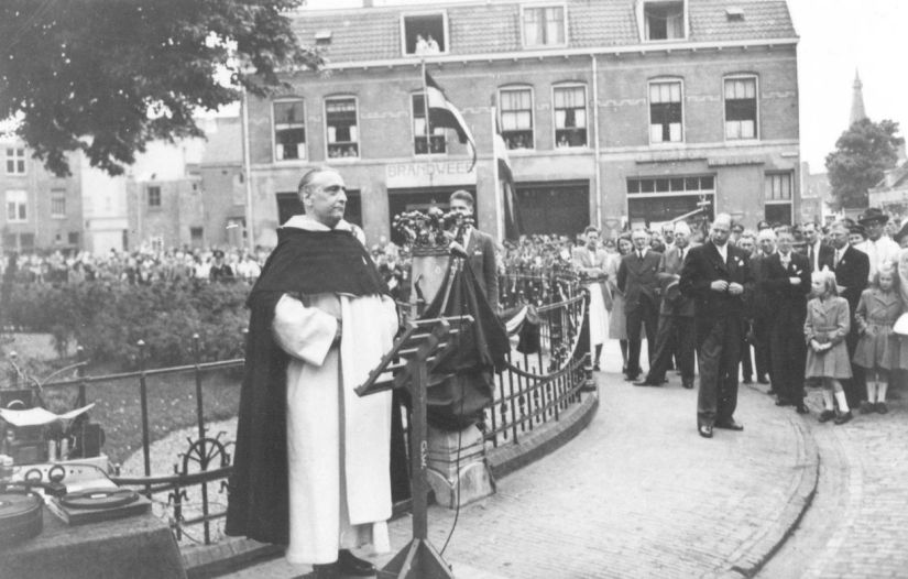 De kroontjes die door de bezetter van het hek bij de Wilhelminaboom waren verwijderd, worden opnieuw geplaatst. Pater Daniëls die de boom als 12-jarige in 1898 plantte, houdt een toespraak, Hertogplein, 24/7/1948 (F55950 RAN)