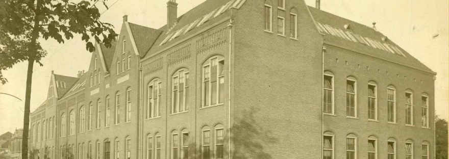 De eerste Nijmeegse Ambachtsschool, opgericht door de Vereeniging Ambachtsonderwijs voor Nijmegen in 1901 en (aansluitend) gebouwd in opdracht van het gemeentebestuur naar ontwerp van gemeentearchitect ir. Jan Jacob Weve. Op de voorgrond de rails van de kolentram voor het vervoer van de steenkool van het station naar de Centrale aan de Waalkade, Nieuwe Marktstraat 12, 1919 (Born via F38489 RAN)