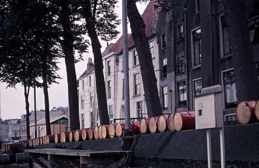 Achterzijde van woningen en bedrijfspanden aan de Lage Markt met links Touwslagerij Reijnen, gezien vanaf de kade. Op de voorgrond de vroegere Waalwal met de opslag van vaten met afgewerkte olie van de firma van Pelt, 1955 (Jeroen van Lith via D975 RAN CC0 vens Auteursrechthouder)