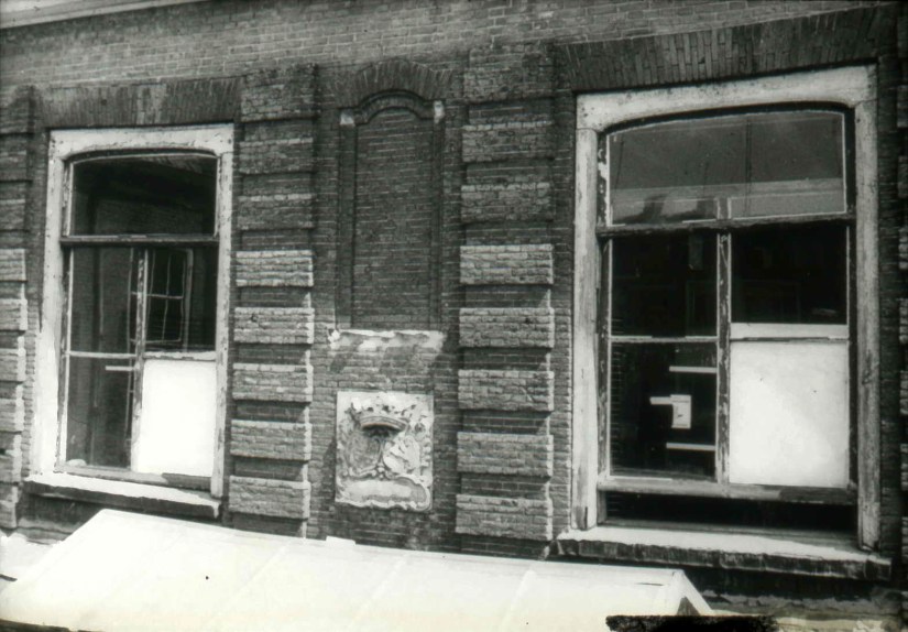 De binnenplaats van het Hof van Batenburg met onder de blinde pui de wapensteen met het alliantiewapen van de families (Johan Michiel) Roukens en (Agneta Jannetta) Verspijck, met de tekst : Ex Invidia et Favore 1751 ( vertaling : Als gevolg van haat en begunstiging). Tegenwoordig is de gevelsteen ingemetseld in een pand aan de Ridderstraat , op de plek van het Hof van Batenburg, het woonhuis van Roukens-Verspijck, Ridderstraat, 1961 (dr. Jan Brinkhoff via D583 RAN CC0 tevens Auteursrechthouder)