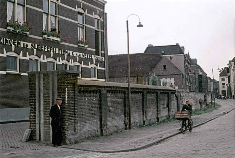 Oude keermuur op de kade ter hoogte van de Vosstraat met voorraan links de (af te sluiten) opening voor het doorgaande verkeer. De muur maakte deel uit van de hoogwaterkering, die - net zoals ook nu nog - de (beneden)stad bij hoog waterpeil van de rivier de Waal moest beschermen. Direct achter de muur de Achter de Vismarkt en het bedrijfspand van Verhuizingen en Sleeperij Firma C. van Wezel, nu volledig gesloopt, 1955 (Jeroen van Lith via F68646 RAN CC0 tevens Auteursrechthouder)