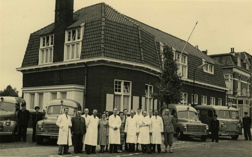 Groepsfoto met het personeel van de Gemeentelijke Geneeskundige en Gezondheidsdienst (GG&GD - GGD) voor de vestiging, Sloetstraat 14, 1954-1955 (Fotopersbureau Gelderland via F38569 RAN CCBYSA Auteursrechthouder J.F.M. Trum; het bijschrift vermeldt ook alle namen)