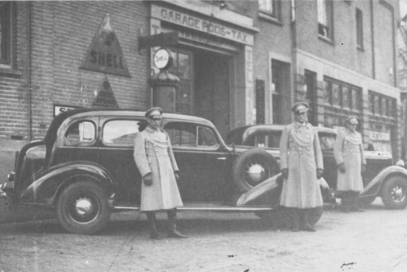 	Drie chauffeurs van garagebedrijf Poos die opgesteld staan voor hun wagens. Van links naar rechts: onbekend, de heer Poos en de heer Pijpers. Rechts het Café-Restaurant Hotel Royal van de Wed. E.W. Poos- Aengenent (op de hoek van de Prins Hendrikstraat 40-42), Waldeck Pyrmontsingel 4 Altrade, 1936 (F15996 RAN)