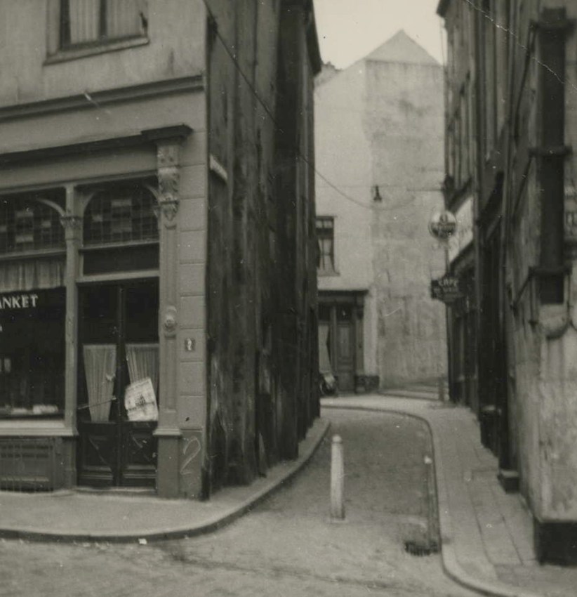 Blik in de Achter de Hoofdwacht, het smalle straatje dat de Smidstraat met de Grote Markt verbindt; links het pand van de brood en banketbakker Mulders aan de Kannenmarkt 2, Achter de Hoofdwacht, 1950-1955 (F94221)