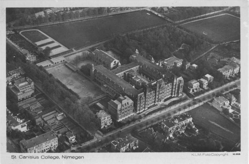 	Vogelvluchtopname van het Sint Canisiuscollege en wat later het Patersbosje zou gaan heten ; aan de Berg en Dalseweg zijn nog onbebouwde terreinen (rechtsonder) ; links in het midden Museum Kam aan de Eleonorastraat (later Museum Kamstraat) ; bovenin de sportvelden van het college aan de Ubbergseveldweg en de Praetoriumstraat, 1930-1931 (KLM Aerocarto via F12698 RAN)